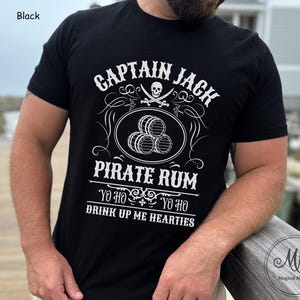 May include: Black t-shirt with a white graphic that reads "CAPTAIN JACK PIRATE RUM" with a skull, crossed swords, and barrels. The text "YO HO YO HO DRINK UP ME HEARTIES" is also included. The shirt is a crew neck.