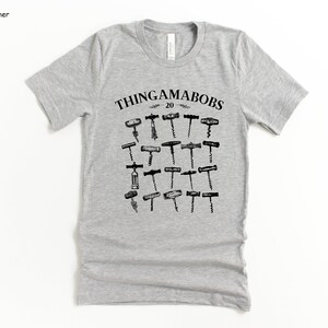 May include: A gray t-shirt with a black graphic of various types of corkscrews. The text "Thingamabobs 20" is printed above the corkscrews.