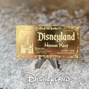 Puede incluir: Un boleto dorado de Disneyland con el texto "Disneyland" en una fuente estilizada. El boleto es para Hannah Rent y es v&aacute;lido por dos d&iacute;as de acceso al parque con la opci&oacute;n "Park Hopper" y los servicios Genie+. El boleto est&aacute; fechado el 21 y 23 de junio de 2022.