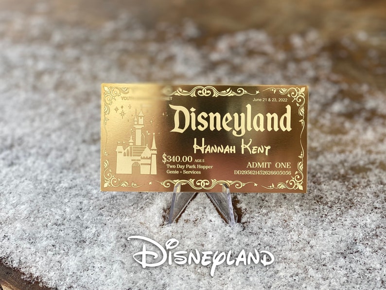 Puede incluir: Un boleto dorado de Disneyland con el texto "Disneyland" en una fuente estilizada. El boleto es para Hannah Rent y es v&aacute;lido por dos d&iacute;as de acceso al parque con la opci&oacute;n "Park Hopper" y los servicios Genie+. El boleto est&aacute; fechado el 21 y 23 de junio de 2022.