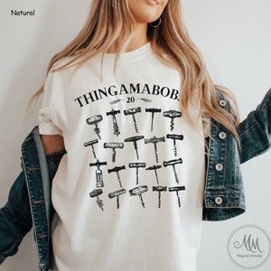 May include: A white t-shirt with a black graphic of the text "Thingamabob 20" and a collection of vintage corkscrews.