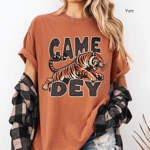 Peut inclure: Un t-shirt couleur rouille avec un motif de tigre et le texte "GAME DAY".