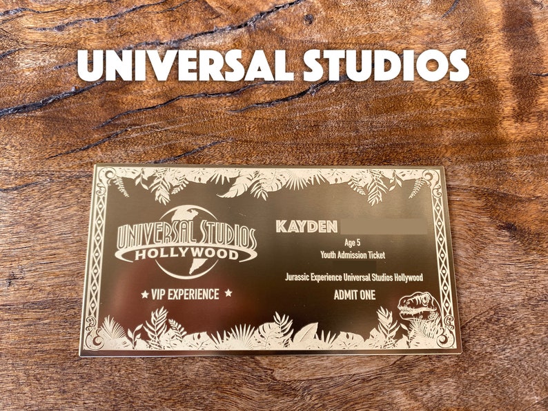 Puede incluir: Un boleto dorado de experiencia VIP de Universal Studios Hollywood con un gr&aacute;fico de dinosaurio. El boleto es para una admisi&oacute;n juvenil y es para Kayden, de 5 a&ntilde;os. El texto "ADMIT ONE" est&aacute; impreso en el boleto.