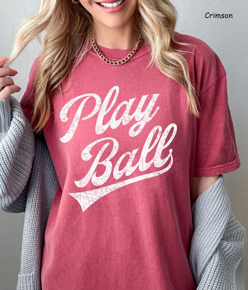 K&ouml;nnte beinhalten: Ein T-Shirt in Rotbraun mit einem wei&szlig;en Vintage-Grafikdruck, auf dem "Play Ball" steht.