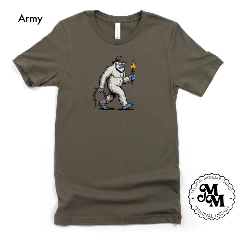 Peut inclure: T-shirt vert arm&eacute;e avec une illustration de dessin anim&eacute; d'un y&eacute;ti blanc portant un chapeau et tenant une torche. Le y&eacute;ti marche et a une corde bleue attach&eacute;e &agrave; sa taille. Le texte "Army" est en haut &agrave; gauche.