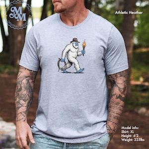Peut inclure: T-shirt gris chin&eacute; avec un dessin d'un y&eacute;ti portant un chapeau, une torche et une corde. Le t-shirt porte le texte "Magical Monda Market Original Design" en haut &agrave; gauche. Info mod&egrave;le : Taille XL, Hauteur : 188 cm, Poids : 102 kg.