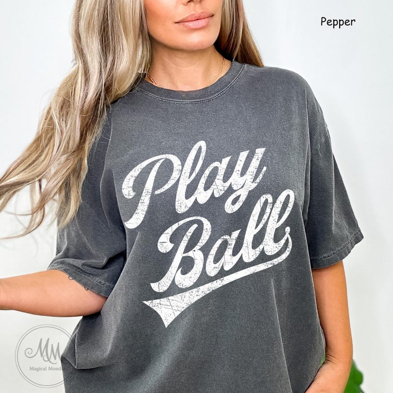 K&ouml;nnte beinhalten: Ein graues T-Shirt mit dem Text "Play Ball" in Wei&szlig;, mit abgenutztem Schriftzug. Das Shirt hat einen Vintage-Look und -Feel.