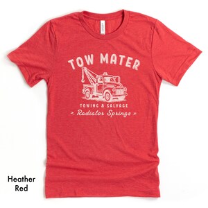 Pu&ograve; includere: T-shirt rosso melange con grafica bianca di un carro attrezzi e le parole "TOW MATER" sopra. Sotto il camion le parole "TOWING & SALVAGE" e "Radiator Springs". La maglietta &egrave; in materiale morbido.