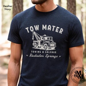 Pu&ograve; includere: T-shirt blu navy con grafica bianca di un carro attrezzi e la scritta "TOW MATER TOWING & SALVAGE Radiator Springs". La maglietta ha girocollo e maniche corte. Il design &egrave; in stile vintage.