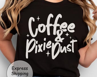 Può includere: T-shirt nero con la scritta bianca "Coffee & Pixie Dust" con stelle. Il testo è scritto in corsivo. La maglietta è abbinata a jeans blu.