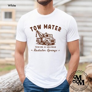 Pu&ograve; includere: T-shirt bianco con grafica marrone di un carro attrezzi e la scritta "TOW MATER TOWING & SALVAGE Radiator Springs". La maglietta ha girocollo e maniche corte. Il design &egrave; in stile vintage.