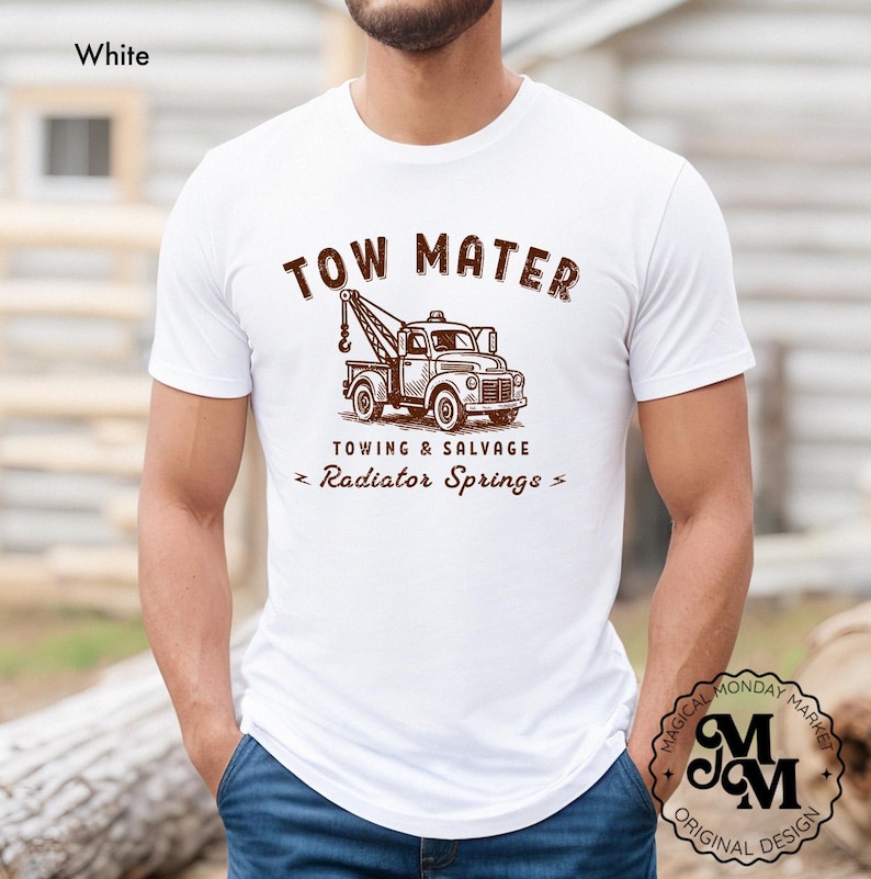 Pu&ograve; includere: T-shirt bianco con grafica marrone di un carro attrezzi e la scritta "TOW MATER TOWING & SALVAGE Radiator Springs". La maglietta ha girocollo e maniche corte. Il design &egrave; in stile vintage.