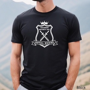 May include: Black t-shirt with a white graphic. The graphic includes a shield design with a crown, crossed swords, and the text "Charming Security Inc." and "Royal Guard". The t-shirt has short sleeves.