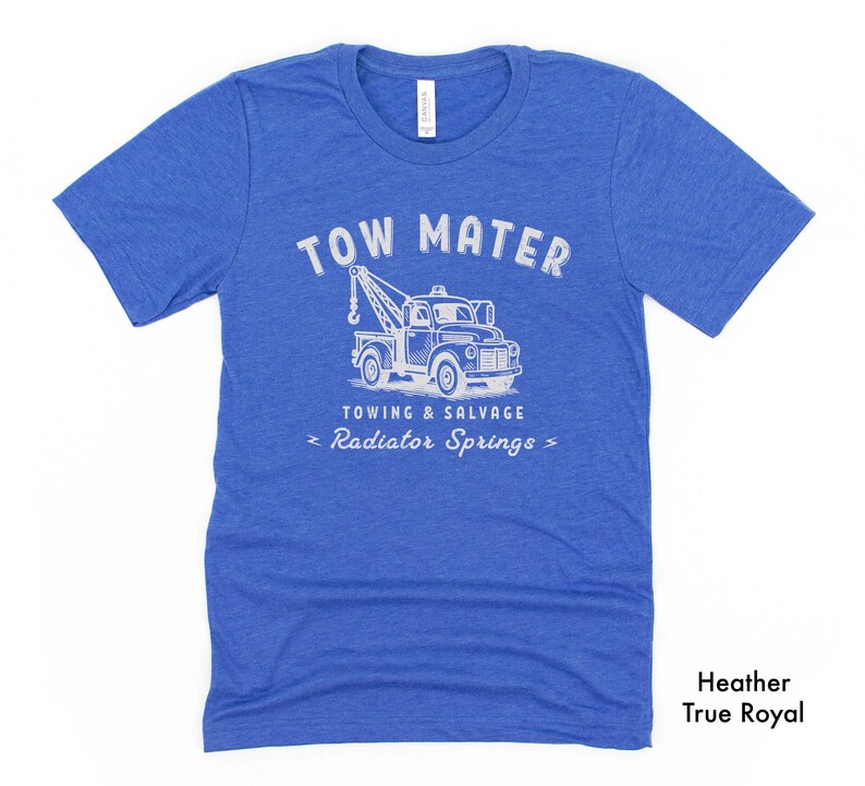 Pu&ograve; includere: T-shirt blu melange con grafica bianca di un carro attrezzi. Il testo sopra il camion recita "TOW MATER" e sotto "TOWING & SALVAGE" e "Radiator Springs". La maglietta &egrave; etichettata "Heather True Royal".