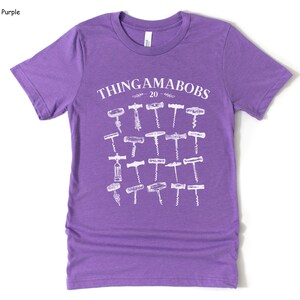 May include: Purple short-sleeved t-shirt with a white graphic of the text "THINGAMABOBS 20" and a collection of 20 different vintage corkscrews.