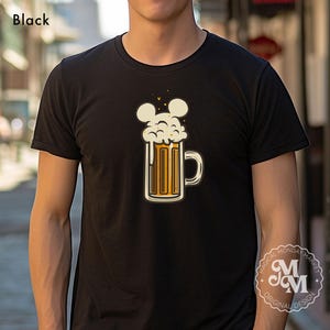 May include: A black short-sleeved t-shirt featuring a graphic of a beer mug with a thick, foamy head shaped like three circles. The text "Black" appears in the top left corner, and a circular logo with "Magical Monday Market" is visible.