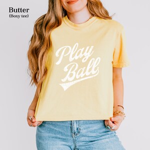 K&ouml;nnte beinhalten: Ein gelbes, locker sitzendes T-Shirt mit einem wei&szlig;en Vintage-Grafikdruck, auf dem "Play Ball" steht.