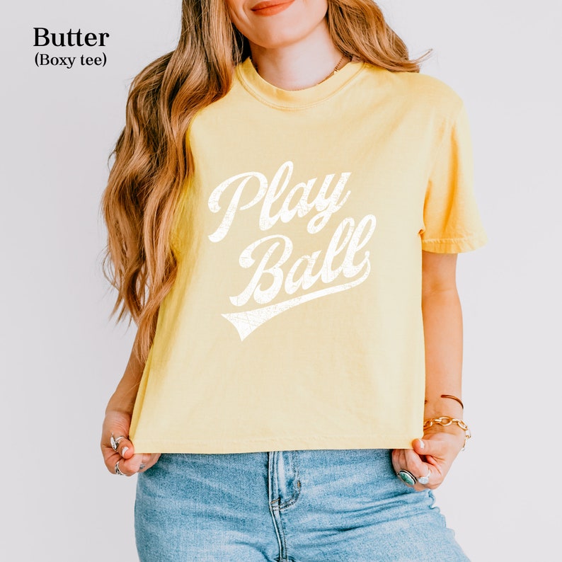 K&ouml;nnte beinhalten: Ein gelbes, locker sitzendes T-Shirt mit einem wei&szlig;en Vintage-Grafikdruck, auf dem "Play Ball" steht.