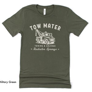 Pu&ograve; includere: T-shirt verde militare con grafica bianca usurata di un carro attrezzi e la scritta "TOW MATER TOWING & SALVAGE RADIATOR SPRINGS". La maglietta &egrave; realizzata in materiale morbido.