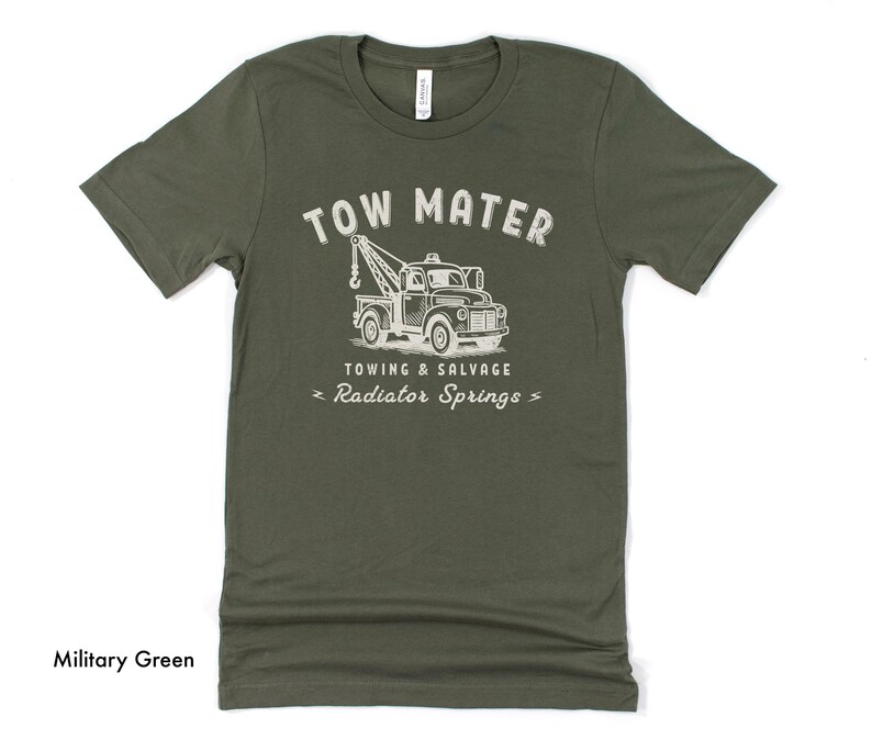 Pu&ograve; includere: T-shirt verde militare con grafica bianca usurata di un carro attrezzi e la scritta "TOW MATER TOWING & SALVAGE RADIATOR SPRINGS". La maglietta &egrave; realizzata in materiale morbido.