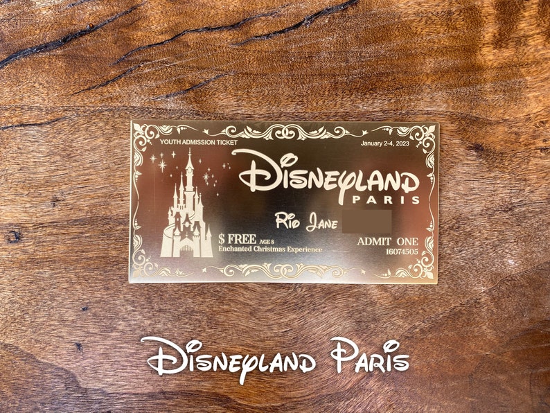 Puede incluir: Un boleto dorado de Disneyland Par&iacute;s con el texto "YOUTH ADMISSION TICKET", "January 2-4, 2023", "DISNEYLAND PARIS", "RID JANE", "$ FREE AGES", "Enchanted Christmas Experience", "ADMIT ONE" y "16074505". El boleto presenta una silueta del castillo de la Bella Durmiente.