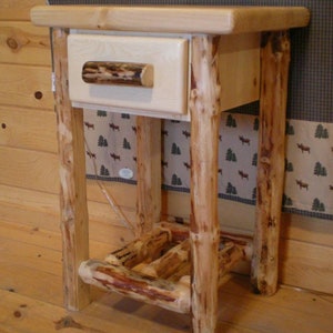 May include: A rustic wooden end table with a single drawer and a natural bark drawer pull. The table has a natural wood finish and is supported by four sturdy legs.