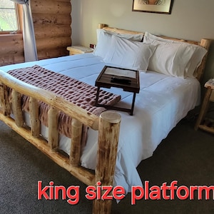 May include: A king size platform bed frame made of natural wood with a white bedspread and a small wooden side table.