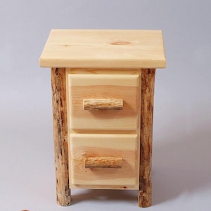 May include: A light-colored wooden nightstand featuring a flat rectangular top and two stacked drawers. The side supports and drawer handles are crafted from natural, unrefined logs with visible bark, contrasting with the smooth light wood finish.