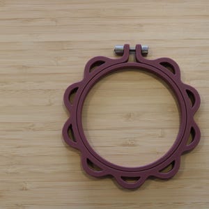 Op de afbeelding: Een cirkelvormige borduurring in een gedempte mauve kleur met een geschulpte buitenrand en decoratieve uitsparingen. Het frame bevat een zilverkleurige metalen spanschroef aan de bovenkant om de ringen stevig op elkaar te klemmen.