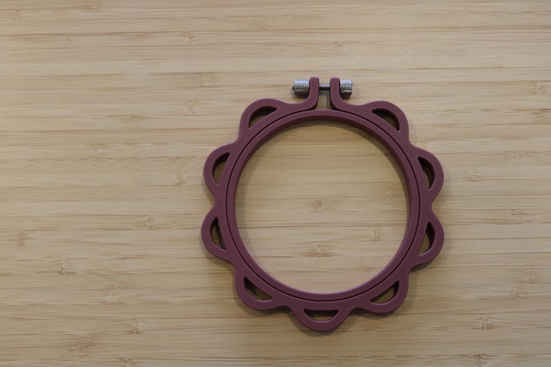 Op de afbeelding: Een cirkelvormige borduurring in een gedempte mauve kleur met een geschulpte buitenrand en decoratieve uitsparingen. Het frame bevat een zilverkleurige metalen spanschroef aan de bovenkant om de ringen stevig op elkaar te klemmen.