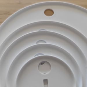 May include: A set of four nested white circular plastic discs of varying sizes, each featuring a centered circular hole and a small rectangular cutout at the bottom. A white plastic stand is positioned to the left of the stacked discs.