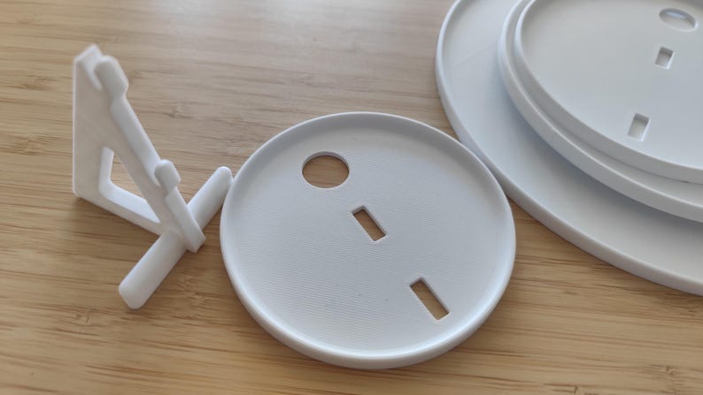 May include: A white plastic display stand with a triangular support structure and a set of three circular white plastic plates. Each plate features a central circular cutout and two rectangular slots, designed for assembly with the display stand.
