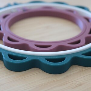 Op de afbeelding: Een set van drie in elkaar passende ronde borduurringen met een geschulpte rand. De grootste buitenste ring is donkerblauwgroen, de middelste ring is wit en de kleinste binnenste ring is gedempt mauve, allemaal met een gladde, matte afwerking.