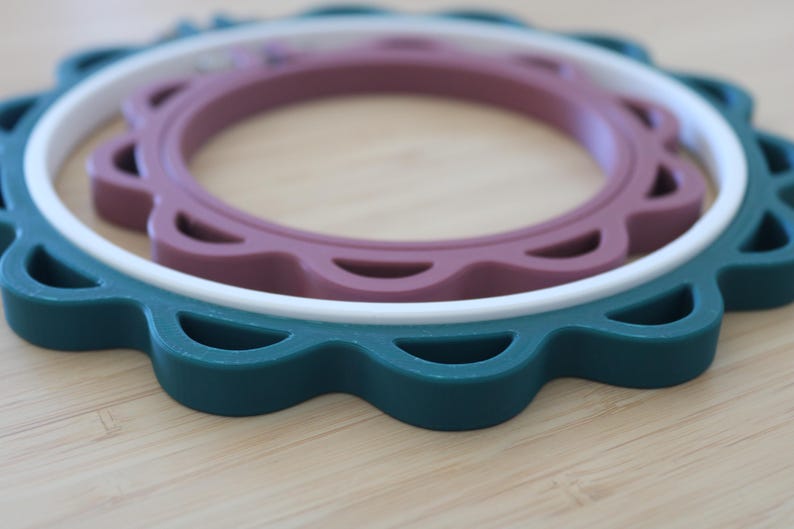 Op de afbeelding: Een set van drie in elkaar passende ronde borduurringen met een geschulpte rand. De grootste buitenste ring is donkerblauwgroen, de middelste ring is wit en de kleinste binnenste ring is gedempt mauve, allemaal met een gladde, matte afwerking.