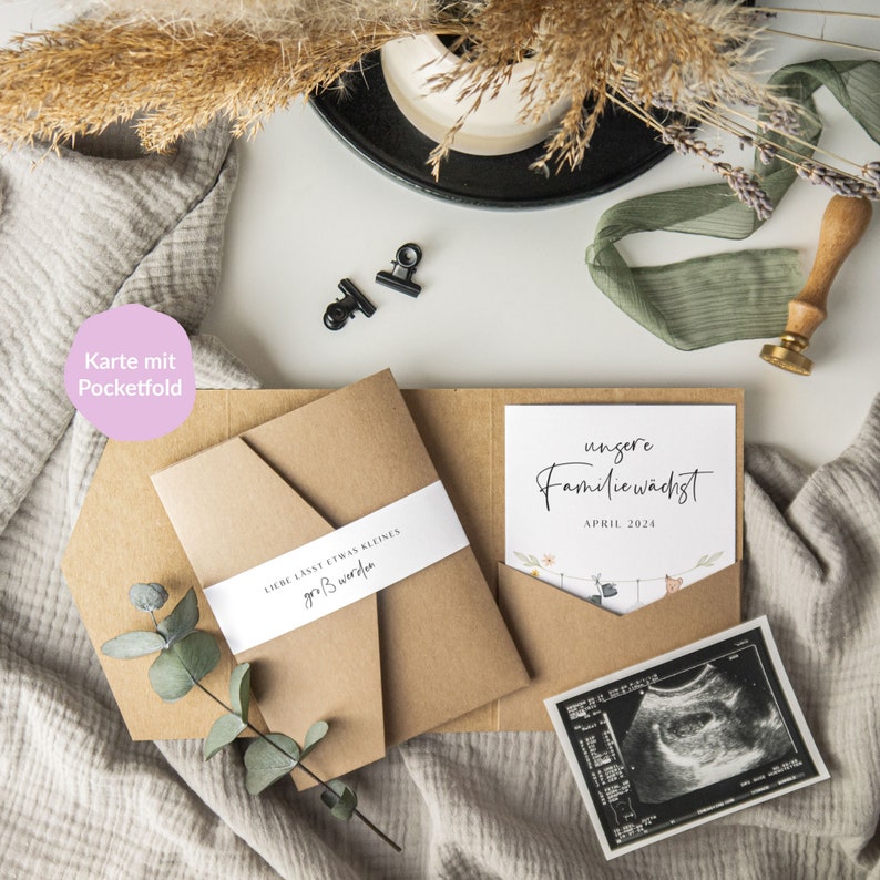 May include: A brown envelope with a white ribbon that says "Liebe lasst etwas kleines gro&szlig; werden" and a smaller envelope inside with a white card that says "unsere Familie w&auml;chst APRIL 2024" and a black and white ultrasound image.