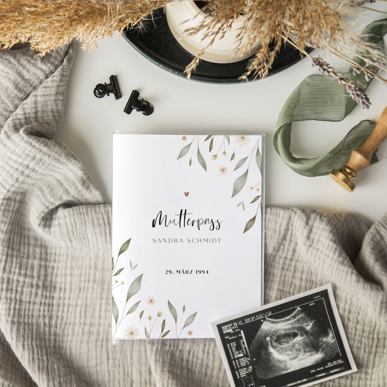 May include: A white book with a floral design and the text "Mutterpass Sandra Schmidt 29. M&auml;rz 1994".