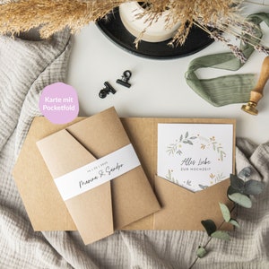 May include: A brown card with a pocketfold design. The card has a white band with the text "14.1.22 | 2023 | Marina & Sandro" and a smaller card inside with the text "Alles Liebe zur Hochzeit" and a floral design.