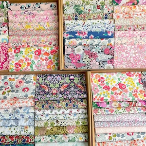 May include: A selection of floral fabric bundles in wooden boxes. The fabrics display a variety of colourful floral patterns, including pink, red, blue, and yellow blooms. The fabrics are neatly folded and stacked, showcasing a range of designs.