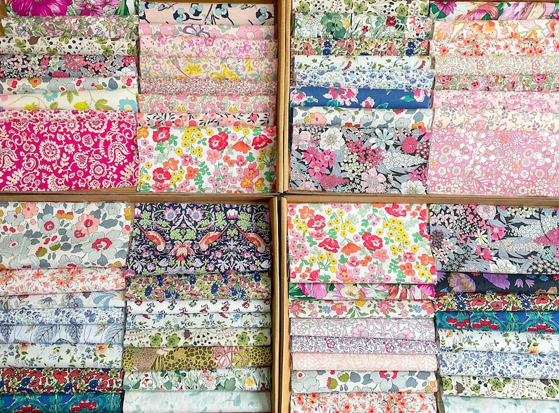 May include: A selection of floral patterned fabrics displayed in wooden boxes. The fabrics showcase a variety of colours, including pink, blue, yellow, and green, with detailed floral designs. The image presents a range of patterns and colours.