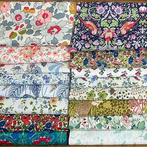 May include: A selection of folded fabric pieces with floral designs. The fabrics display a range of colours, including pink, blue, green, and yellow. Some fabrics have large floral patterns, while others have smaller, more intricate designs. The fabrics appear to be cotton or a similar material.