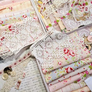 May include: A collection of pink and white fabric scraps, lace, and buttons in a wooden box. The fabrics feature floral patterns and delicate lace trims. The box is filled with various crafting supplies, including ribbons, beads, and other embellishments.