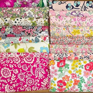 May include: A selection of floral fabric bundles in a range of colours. The fabrics display diverse floral patterns, including pink, white, green, and yellow flowers. The bundles are neatly stacked, showcasing the different designs.