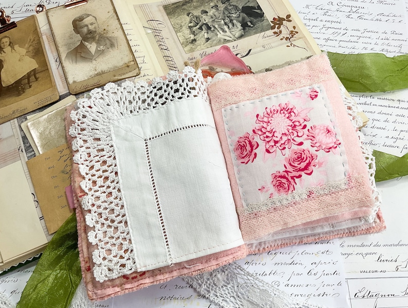 May include: A pink fabric journal with a white lace trim and a floral fabric insert. The journal is open to reveal a white page with a pink floral pattern.