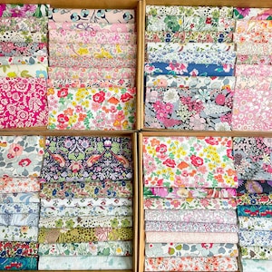 May include: A selection of floral fabric swatches displayed in wooden boxes. The fabrics showcase a variety of colourful floral patterns in pink, red, blue, and green. The swatches are neatly arranged, displaying a range of designs and colours.
