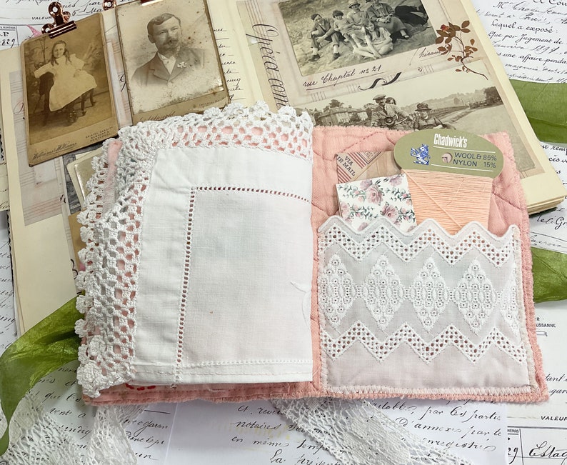 May include: A pink fabric book with a white lace trim and a pocket on the front. The pocket contains a small piece of fabric with a floral pattern and a spool of pink thread. The label on the spool reads "Chadwick's Wool & 88% Nylon 15%".