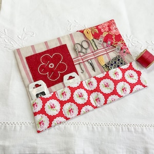 Könnte beinhalten: Ein Nähset mit rot-weißem Blumenmuster, das verschiedene Nähwerkzeuge enthält. Das Set enthält Schere, Nadeln, Faden und Knöpfe. Es hat ein rotes Filzblumen-Design und ist aus Stoff gefertigt.