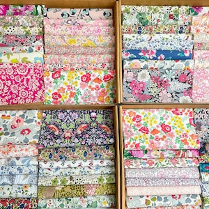 May include: Fabric bundles with floral patterns are displayed in wooden boxes. The fabrics feature a variety of colours, including pink, red, blue, and green, with detailed designs. Suitable for quilting and craft projects.