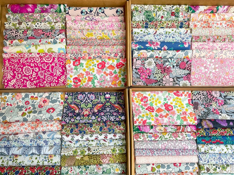 May include: Fabric bundles with floral patterns are displayed in wooden boxes. The fabrics feature a variety of colours, including pink, red, blue, and green, with detailed designs. Suitable for quilting and craft projects.