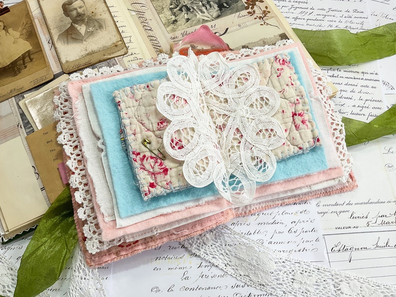 May include: A stack of fabric scraps in various shades of pink, blue, and white, with a delicate white lace overlay. The fabric scraps are arranged in a layered fashion, creating a visually appealing and textured composition.