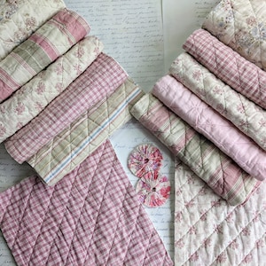 May include: A stack of pink and white quilted fabric scraps with floral and striped patterns. The fabric is arranged in a fan shape on a white surface with handwritten text.